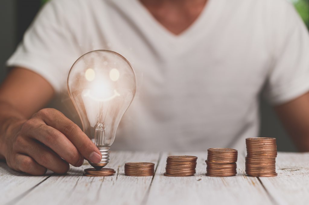 Mann hält Glühbirne, Stapel mit Geld, Energiesparen